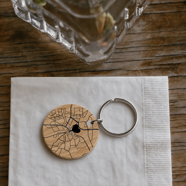 Runder Holz-Schlüsselanhänger mit gravierter Straßenkarte und Herzmarkierung, auf einer weißen Serviette bei einer rustikalen Hochzeitstafel